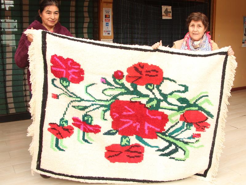 Sra. Sara Mayorga y Sra. Rosa Miranda sosteniendo una alfombra, textil tejido en quelgo (telar horizontal propio de Chiloé).