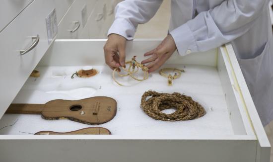Manos acomodan pieza textil -cordón de fibras naturales- en un cajón especialmente acondicionado